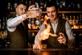 bartender pours drink into glass and another man bartender sets it on fire