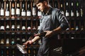 Bartender pours red wine in transparent vessel in cellar