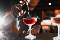 The bartender prepares red alcoholic cocktails at the bar.