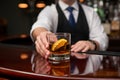 Bartender presents amber liquid glass with orange slice on polished wooden countertop