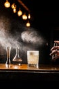 Bartender is spraying whiskey over Penicillin cocktail in the bar. Bartender mixes whiskey, lemon juice, and honey