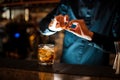 Bartender sprinkling orange peel juice into a cocktail glass