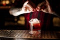 Bartender sprinkling orange peel juice into a cocktail glass filled with strong whiskey drink