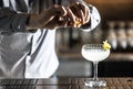 A bartender squeezes a lemon peel and squirts the juice onto a French 75 cocktail drink on the bar counter