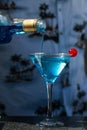 Bartender wearing a tropical shirt pours from a bottle into a glass of Blue Lagoon alcohol cocktail