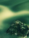 Basalt boulder in blurred mountain rapid stream. Blue blurred waves, milky smoky water with reflections. Royalty Free Stock Photo