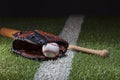 Baseball in a mitt with bat at low angle view on a field with stripe and dramatic lighting and dark background Royalty Free Stock Photo