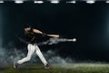 Baseball player with bat taking a swing on grand arena. Ballplayer on dark background in action.