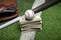 Baseball on top of stack of money with mitt and bat on green field with stripe Royalty Free Stock Photo