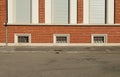 Basement windows on brick wall facade with tarmac sidewalk and urban road in front.