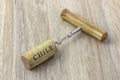 A basic corkscrew with a cork on a wooden table. Name of wine country Chile is written on cork