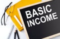 BASIC INCOME text on the blackboard with notepad , pen, pencil Royalty Free Stock Photo