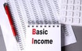 BASIC INCOME text on notebook with chart , pen and calculator