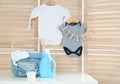 Basket with baby laundry, bottle of detergent and washing powder on white table