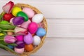 Basket with multi-colored Easter eggs and tulips on a white wooden background. View from above. Copy space. Festive spring banner Royalty Free Stock Photo