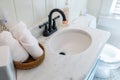 A basket of organized clean rolled white towels on a bathroom counter in a guest bathroom near a sink and toilet.