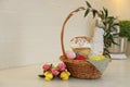 Basket with traditional Easter cake, dyed eggs and flowers on table near white brick wall. Space for text Royalty Free Stock Photo