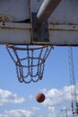 A basketball ball flies into a hoop with a metal net outdoors