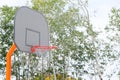 Basketball hoop with backboard in a city park, on a green trees background