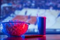 Basketball match on the TV screen. On a wooden table are a glass bowl of popcorn, a carbonated drink in a plastic glass, and a TV