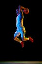 Basketball player doing layup to basket in action against black studio background in mixed neon light. Dynamic shot. Royalty Free Stock Photo