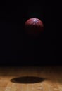 Basketball spot lit suspended in air against black background above hardwood maple court floor