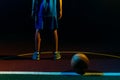 Basketball. A teenage boy in a blue sportswear stands on the Playground with ball. Close up of legs. Black background. Rear view. Royalty Free Stock Photo