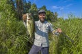 Bass fishing. Big bass fish in hands of pleased fisherman with spinning rod. Largemouth perch at pond