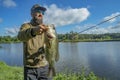 Bass fishing. Large bass fish in hand of pleased bearded fisherman with tackle. Largemouth perch at pond Royalty Free Stock Photo