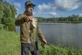 Bass fishing. Large bass fish in hands of pleased bearded fisherman with tackle. Largemouth perch at pond Royalty Free Stock Photo