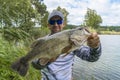 Bass fishing. Large bass fish in hands of pleased fisherman. Largemouth perch at pond Royalty Free Stock Photo