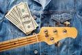 Bass guitar headstock and one hundred dollar bills on denim jeans jacket Royalty Free Stock Photo