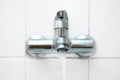 Bath fitting or tap with running water on a white tiled wall in an older bathroom, copy space, selected focus