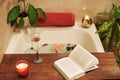 Bath with flower petals. Book, candles and glass of wine on a wood tray. Organic Spa Relaxation in comfort cozy bathroom Royalty Free Stock Photo