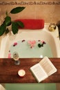 Bath with flower petals. Book, candles and glass of wine on a wood tray. Organic Spa Relaxation in comfort cozy bathroom Royalty Free Stock Photo