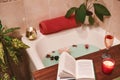 Bath with flower petals. Book, candles and glass of wine on a wood tray. Organic Spa Relaxation in comfort cozy bathroom Royalty Free Stock Photo