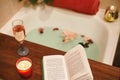 Bath with flower petals. Book, candles and glass of wine on a wood tray. Organic Spa Relaxation in comfort cozy bathroom Royalty Free Stock Photo