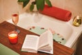 Bath with flower petals. Book, candles and glass of wine on a wood tray. Organic Spa Relaxation in comfort cozy bathroom Royalty Free Stock Photo