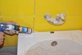 Bath tube installation with Silicone Bathroom Caulk, water tap in the yellow tiled bathroom. Repair bathroom with new bath tube.