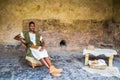 Black reenactor in costume poses as Roman scholar inside stone room with wooden book and worktable inside