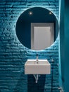 Bathroom with blue bricks wall, square wash basin and round mirror. Minimalist interior.