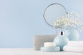 Bathroom decor for female in light soft blue color - circle mirror, silver cosmetic bag, white flowers, towel, soap and vase. Royalty Free Stock Photo