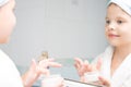 In the bathroom, a girl in a white coat, holds a jar of face cream in her hand and looks in the mirror Royalty Free Stock Photo