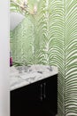 A bathroom with a black cabinet and green and white wallpaper.