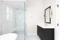 A bathroom with a grey cabinet, gold sconces, and marble shower.