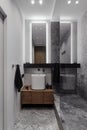 Bathroom in grey tones, stylish in modern design, dark wooden tumble, glass and mirror. Chrome crane. Black towel