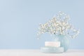 Bathroom interior - ceramic accessories - light blue circle vase, soap with white flowers on white wood table.