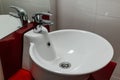 Bathroom interior with round sink and faucet on red stand and white tile background. Royalty Free Stock Photo