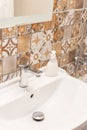 Bathroom interior. Sink, beige ceramic tile, metal faucet, white soap, close-up mirror