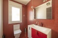 Bathroom with square frameless mirror, wooden chest of drawers and red tiled walls
